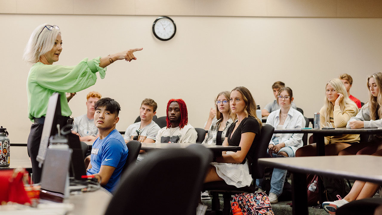 A Professor pointing while lecturing to a classroom of students